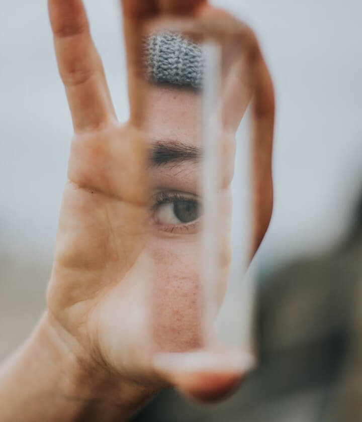 A person’s eye reflected in a narrow handheld mirror.
