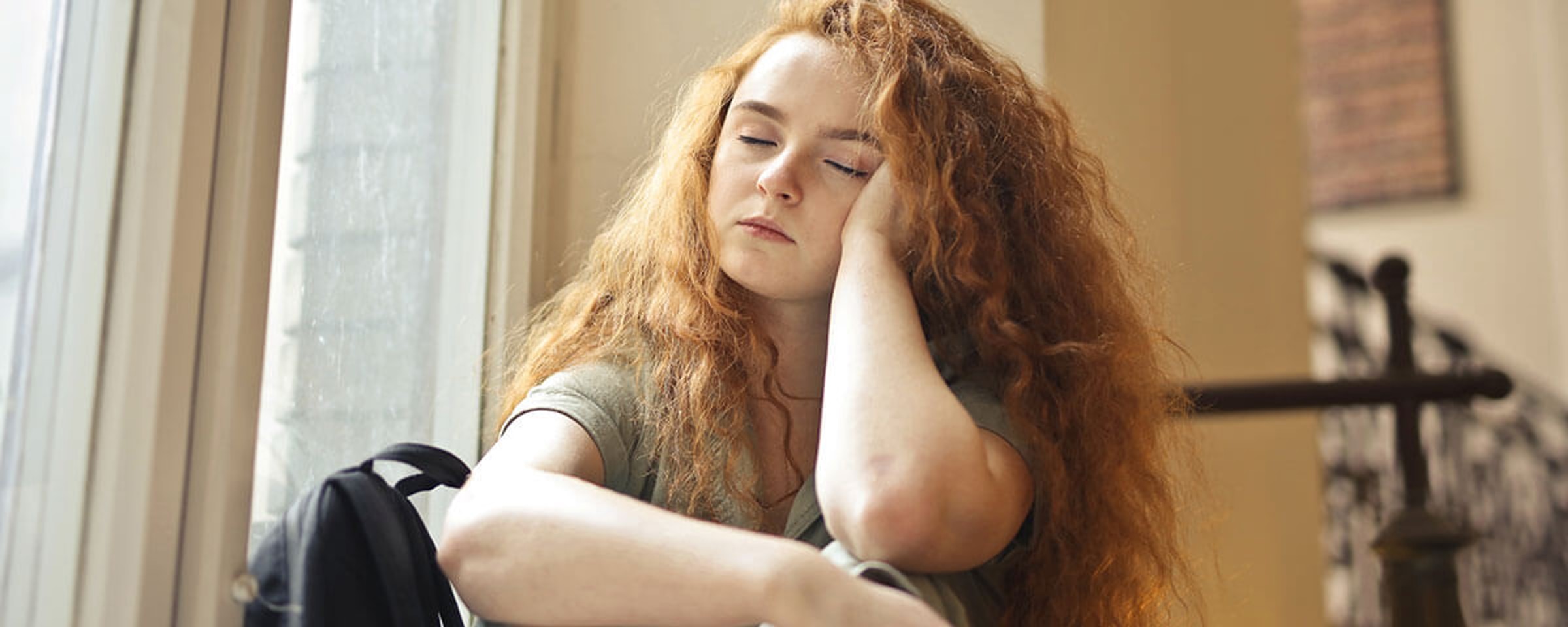 A woman sitting beside a window with her head resting on her hand.