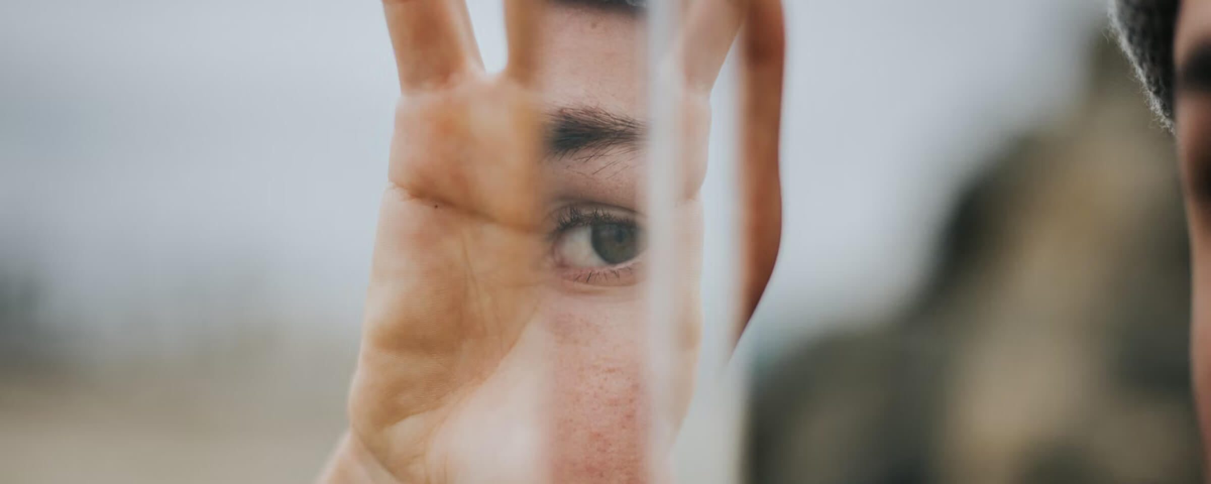 A person’s eye reflected in a narrow handheld mirror.