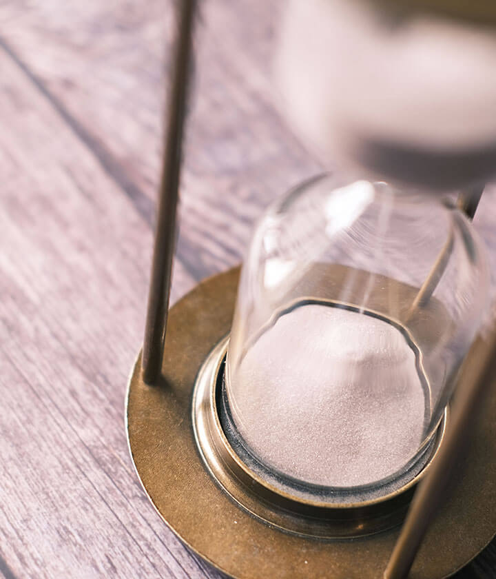 Sand running through a glass hourglass on a wooden table.