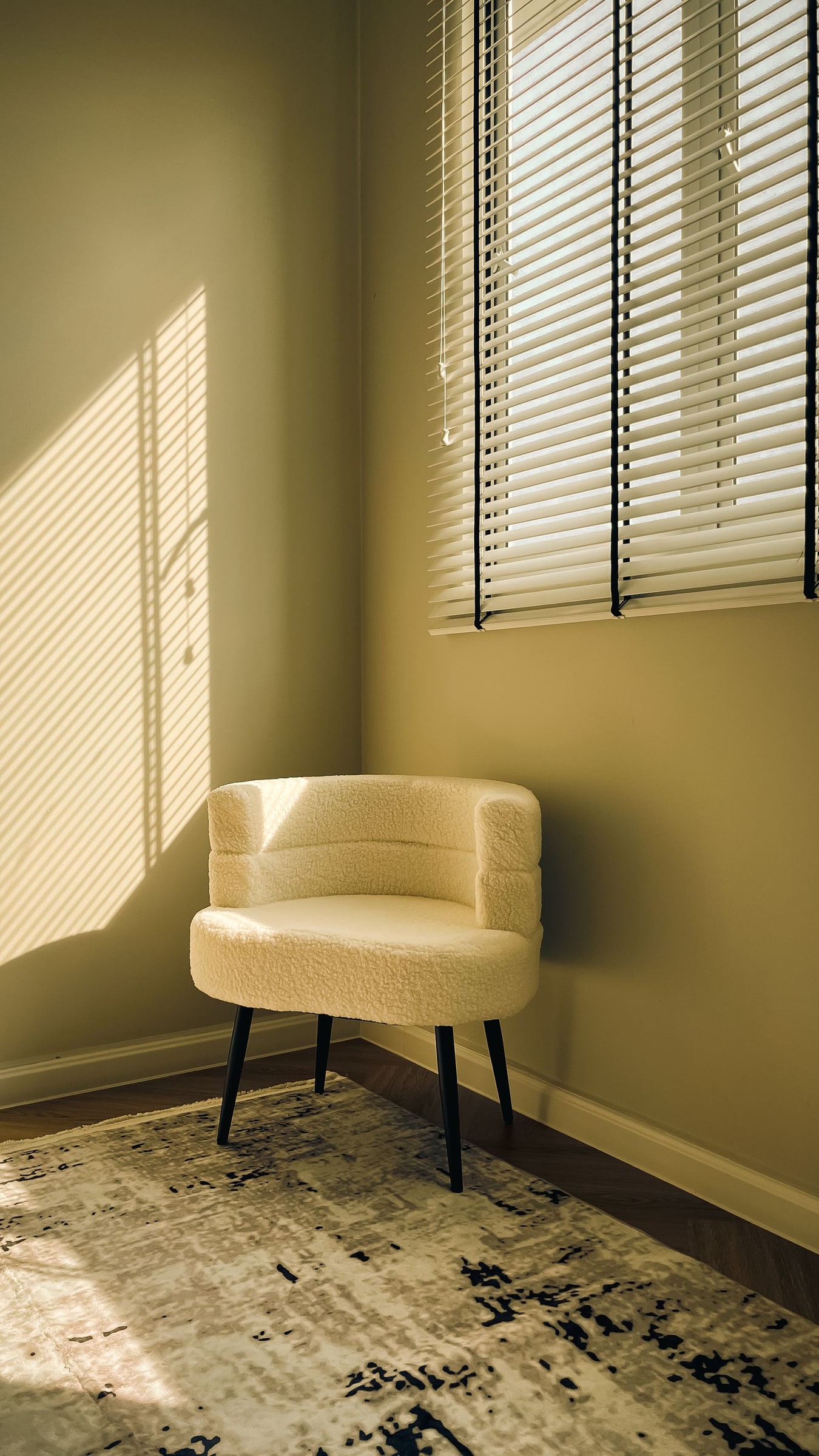 A cream armchair beside a window, with soft shadows cast by the blinds.