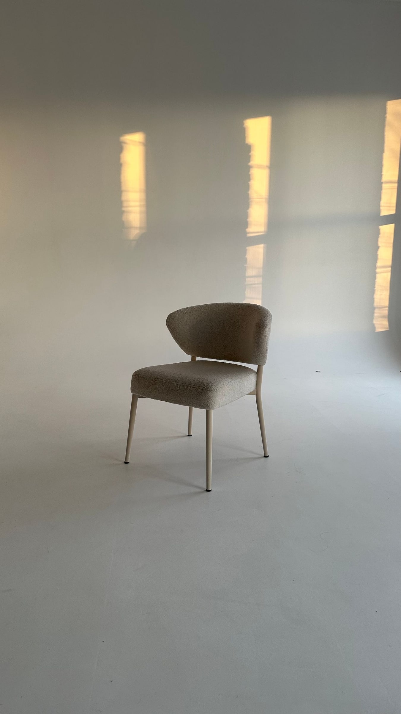 A single upholstered chair in a quiet room, with sunlight falling across the wall.