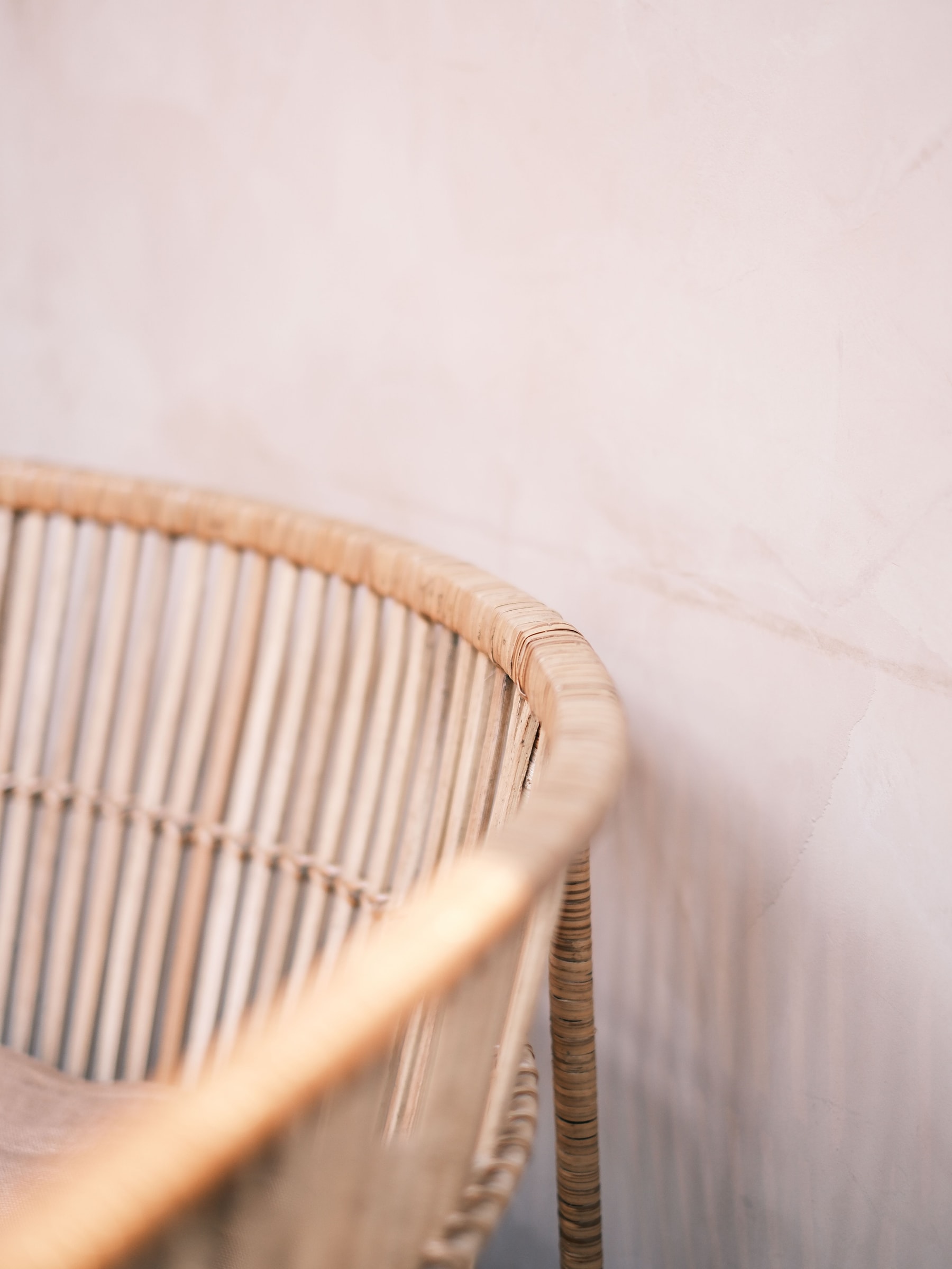 The curved back of a rattan chair against a softly textured blush wall.