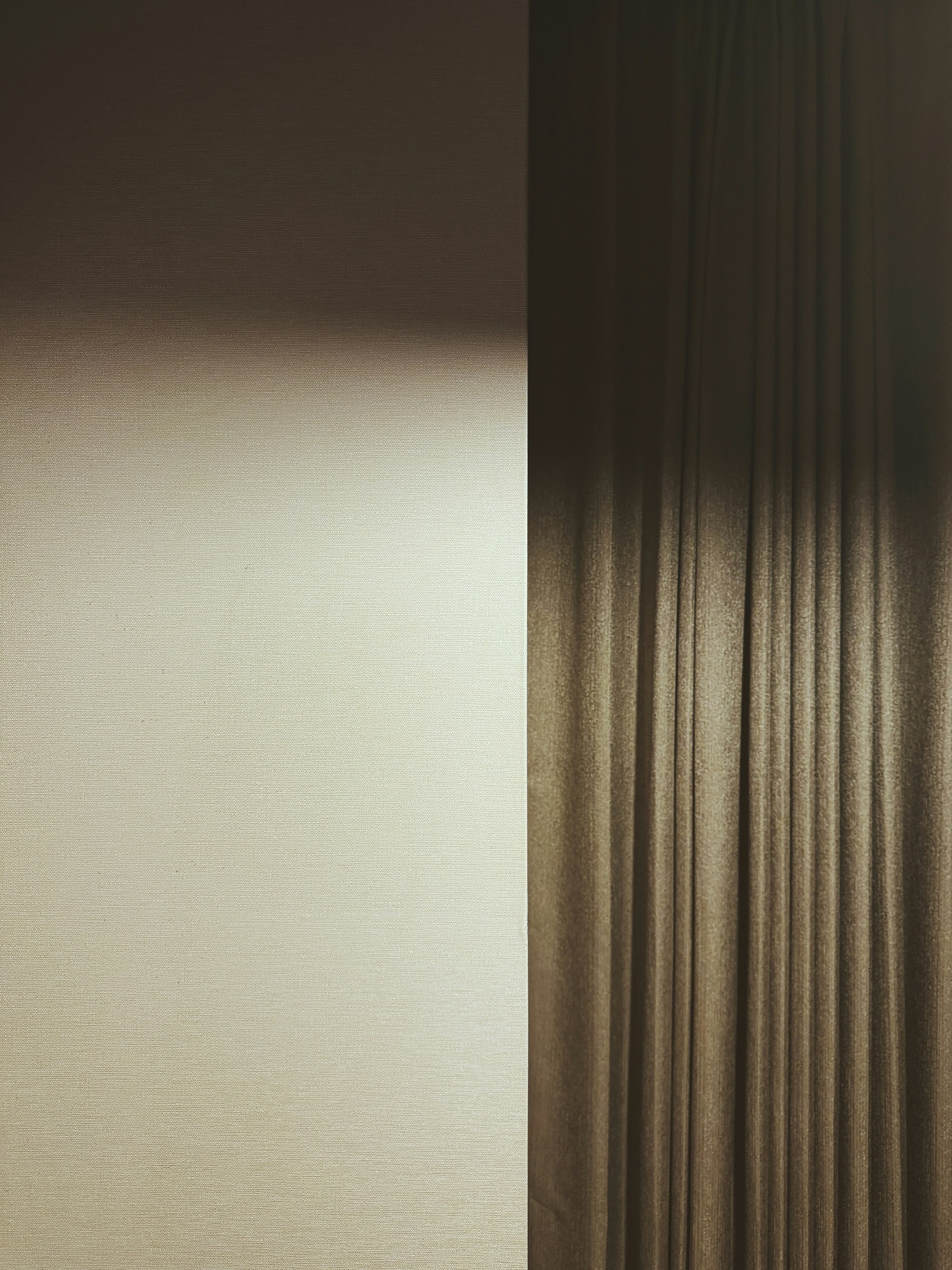 A softly lit cream wall beside a dark brown curtain.