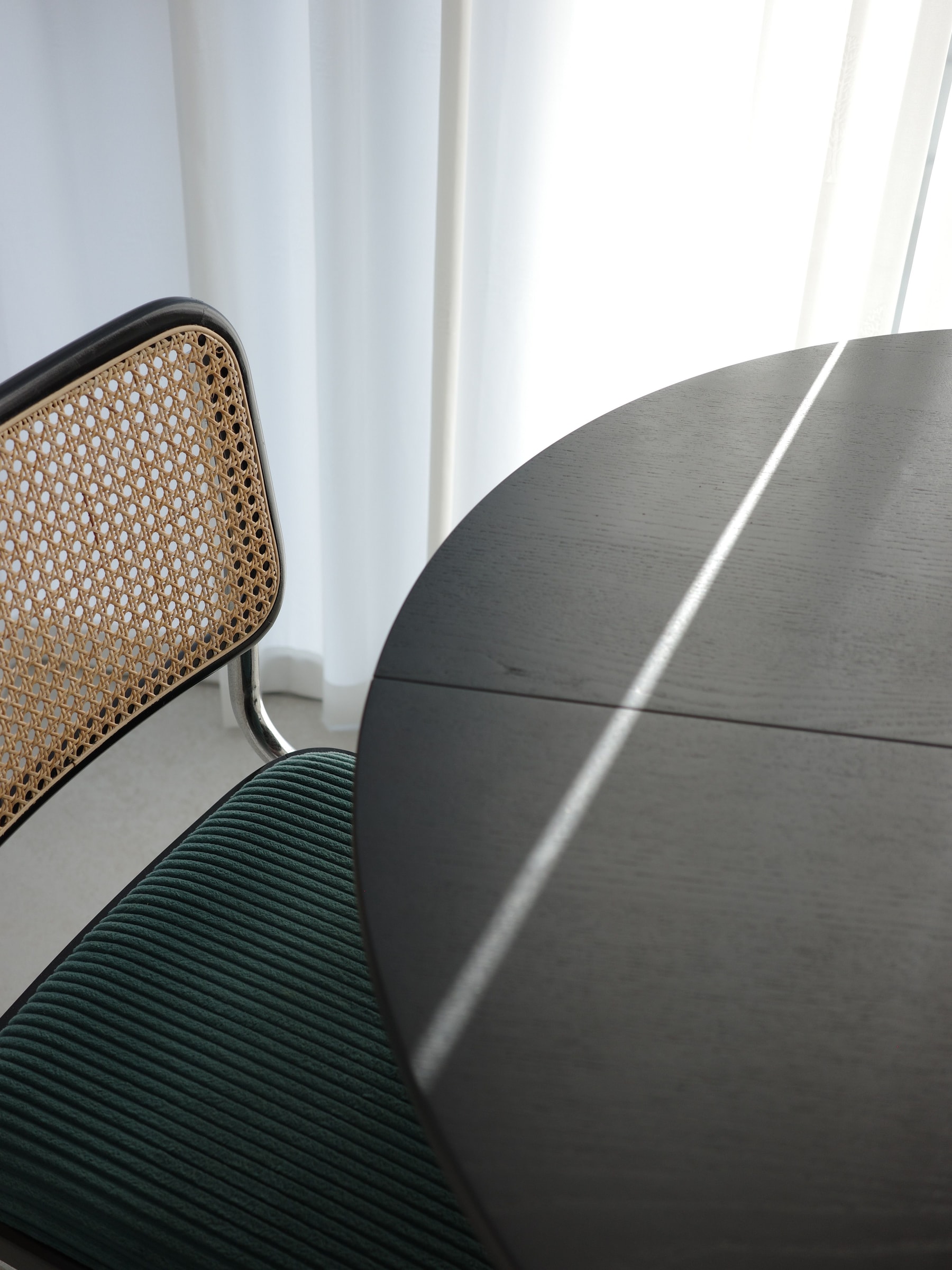A woven-back chair beside a dark round table in narrow beams of sunlight.