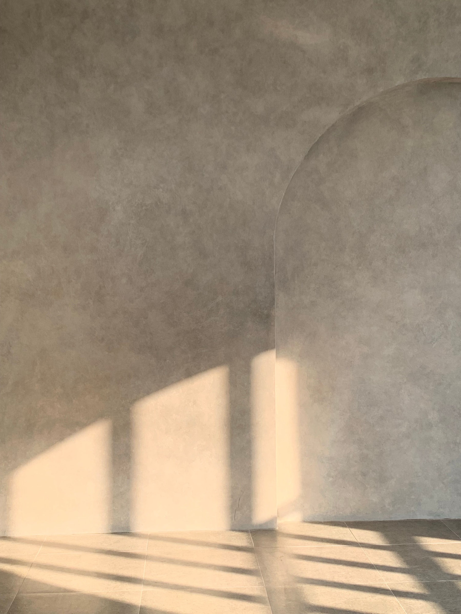 Warm sunlight reaching across a pale plaster wall with a curved arch.