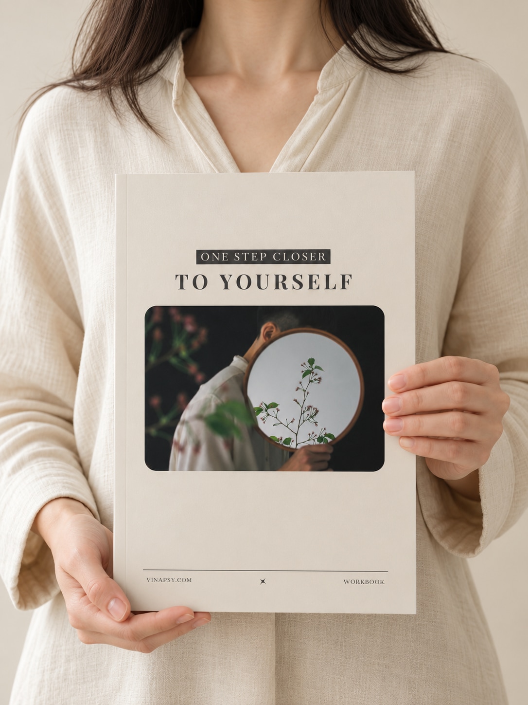 A woman in a cream linen shirt holding the One Step Closer to Yourself workbook.